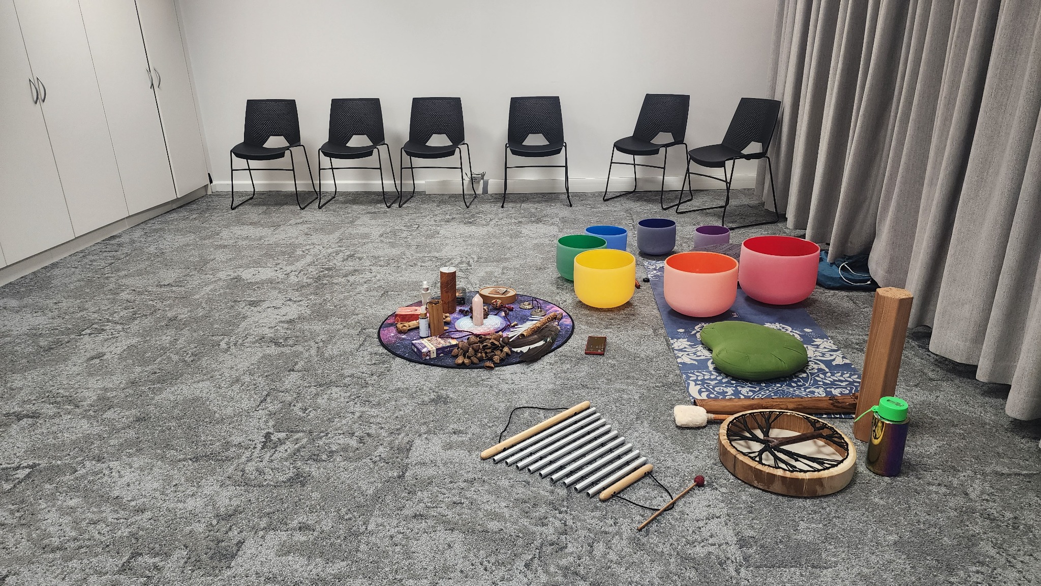 Empty chairs arranged around sound bowls and ceremonial instruments for a private group
