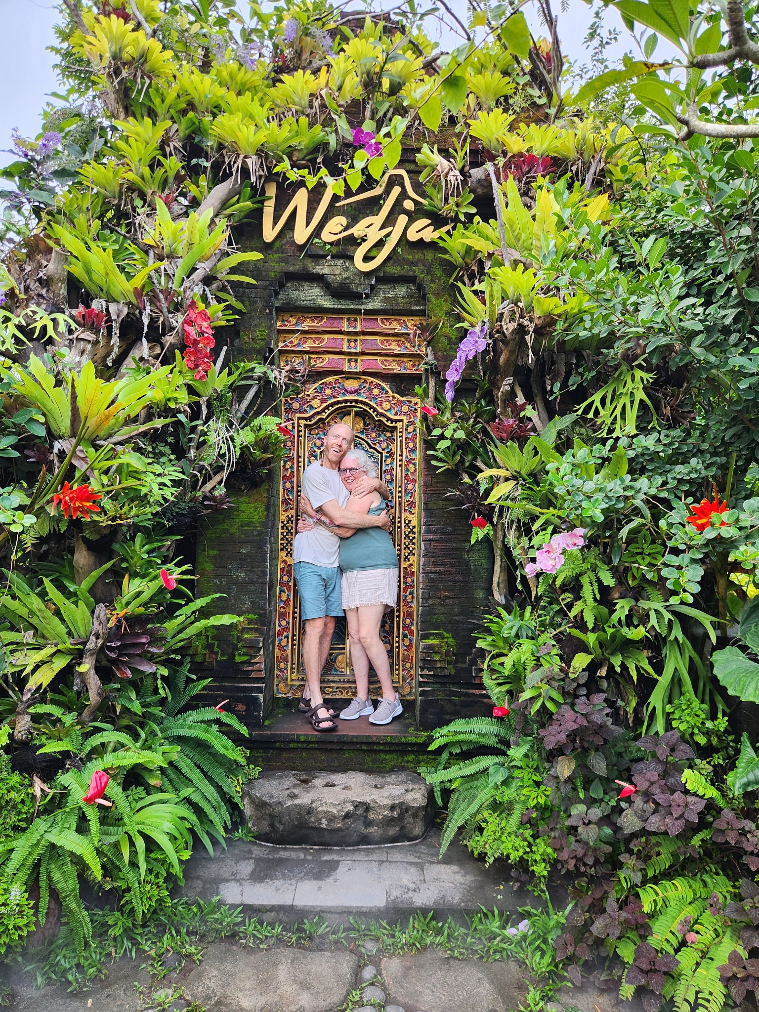 Two retreat guests sharing a joyful moment at a lush Balinese garden entrance